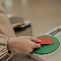 Dłoń zbliża czerwoną kartę do zielonego czytnika na bramce.