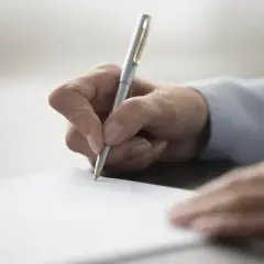 Dłoń pisząca długopisem po białej kartce papieru.