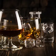 Kilka szklanek z różnymi alkoholami i lodem na drewnianym stole.