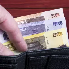 Dłoń wsuwa banknoty o nominałach 5000, 10000 i 20000 do czarnego portfela.
