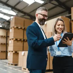 Dwóch specjalistów logistyki omawia coś na tablecie w magazynie pełnym paczek.