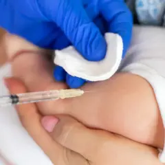 Ręka w niebieskiej rękawiczce wykonuje szczepienia noworodka. Delikatna skóra dziecka, wacik i strzykawka.
