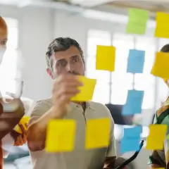 Zespół planuje strategię, wykorzystując karteczki samoprzylepne. Rozważają **outsourcing** zadań, by usprawnić proces.