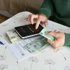 Dłonie trzymające pieniądze, kalkulator i dokumenty ZUS na stoliku.