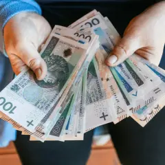 Dłonie trzymające plik polskich banknotów 100 zł.
