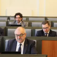 Mężczyźni w garniturach siedzą w rzędach, patrząc na laptopy.