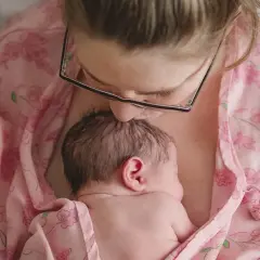 Mama całuje główkę noworodka, otulając go w różowy materiał. To piękny moment kangurowania, budowania więzi.