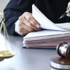 Sędzia w todze przegląda dokumenty, obok waga sprawiedliwości i młotek.