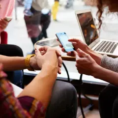 Dwie osoby przy stoliku dyskutują o podatku cyfrowym, jedna pokazuje coś na telefonie, druga ma laptopa.