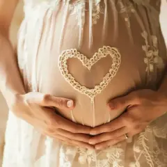 Brzuszek w 7 tygodniu ciąży, otulony koronkowym sercem. Dłonie mamy i taty czule obejmują przyszłe życie.