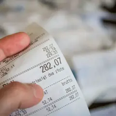 Dłoń trzyma paragon z widoczną kwotą 282,07 zł.