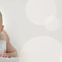 Uśmiechnięte niemowlę z otwartymi ustami leży na brzuchu na jasnym tle z okręgami.