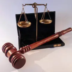 Młotek sędziowski i waga szalkowa na tle otwartego czarnego etui.