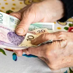 Dłonie starszej osoby liczą pieniądze. Może to być dodatek opiekuńczy po 80 roku życia, zapewniający wsparcie finansowe.