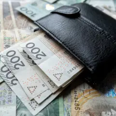Czarny portfel na stosie polskich banknotów 100 i 200 zł.