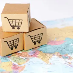 Trzy kartony z ikonami wózków sklepowych na mapie świata, symbolizujące globalny eksport i handel.