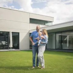 Rodzina z dzieckiem na trawniku przed nowoczesnym domem.
