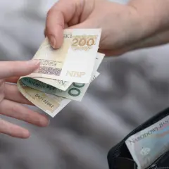Dwie ręce przekazują sobie polskie banknoty 200 zł i 500 zł z portfela.
