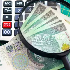 Kalkulator, szkło powiększające i banknoty 100 zł na zielonej macie.