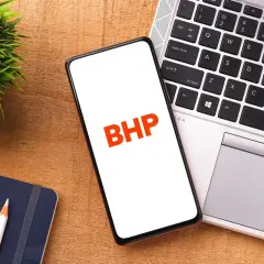 Telefon z napisem BHP na ekranie, obok laptopa, notatnika i rośliny.