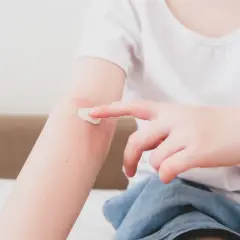 Dziecko smaruje kremem zaczerwienioną skórę na ramieniu, łagodząc objawy azs u dzieci.