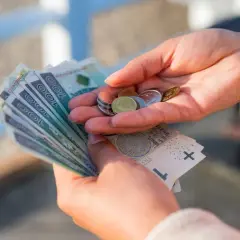 Dłonie trzymające polskie banknoty i monety.