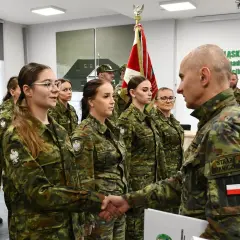 Uroczystość w Straży Granicznej: funkcjonariuszka ściska dłoń przełożonemu, w tle inni funkcjonariusze.