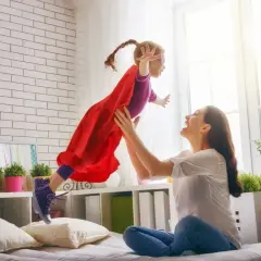 Radosna dziewczynka w stroju superbohaterki lata w górę, złapana przez uśmiechniętą mamę. To wspaniałe, babciowe chwile pełne zabawy.