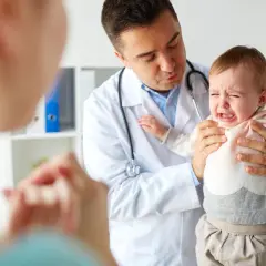 Lekarz uspokaja płaczące dziecko, które przechodzi trudny skok rozwojowy. Mama patrzy z troską.