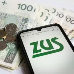 Telefon z logo ZUS na ekranie, obok polskie banknoty i monety.