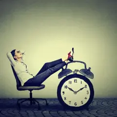 Kobieta w okularach odpoczywa na krześle z nogami na budziku. Czas wolny od pracy 1 maja.