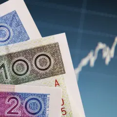 Polskie banknoty 50, 100 i 20 zł na tle wykresu giełdowego. Symbolizują bezpieczeństwo finansowe, jak bankowy fundusz gwarancyjny.