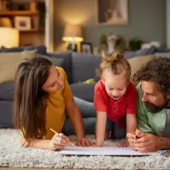 Rodzina rysuje kredkami na dywanie w salonie.