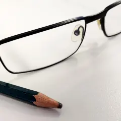 Okulary i ołówek na białym tle.