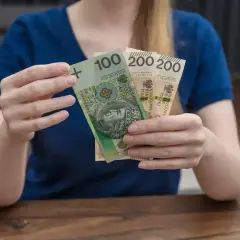 Dłonie trzymające polskie banknoty: 100 zł i dwa razy po 200 zł.