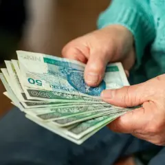 Dłonie starszej osoby trzymające stos polskich banknotów.