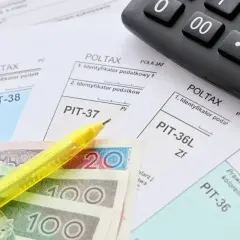 Formularze PIT, polskie banknoty, żółty długopis i kalkulator.