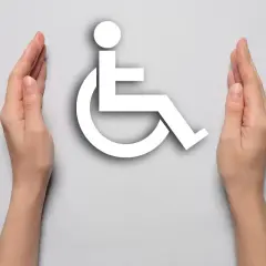 Dwie dłonie otaczają biały symbol osoby na wózku inwalidzkim na jasnoszarym tle.