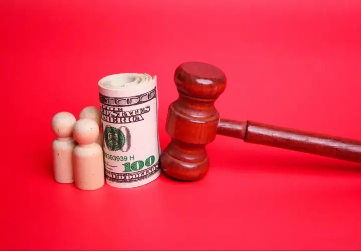 Drewniany młotek sędziowski, zwinięty banknot 100 dolarów i trzy drewniane figurki symbolizujące rodzinę. Pytanie: do kiedy alimenty na dziecko?