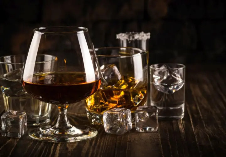 Kilka szklanek z różnymi alkoholami i lodem na drewnianym stole.