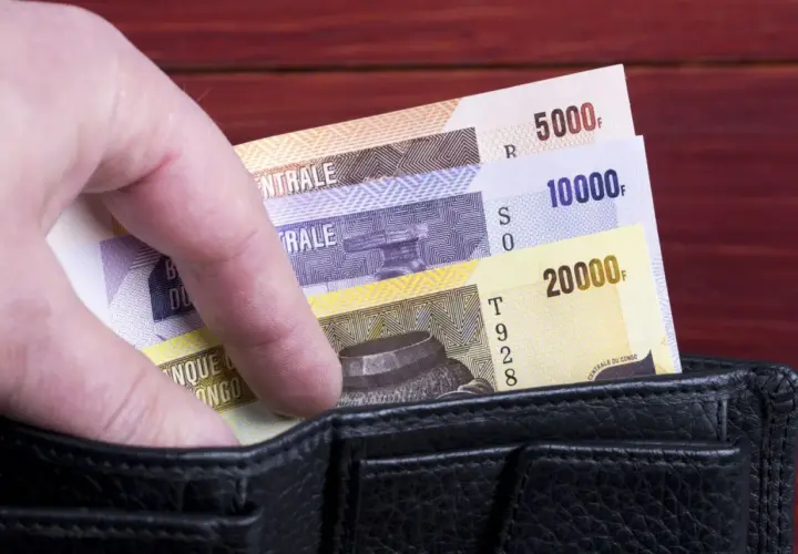 Dłoń wsuwa banknoty o nominałach 5000, 10000 i 20000 do czarnego portfela.