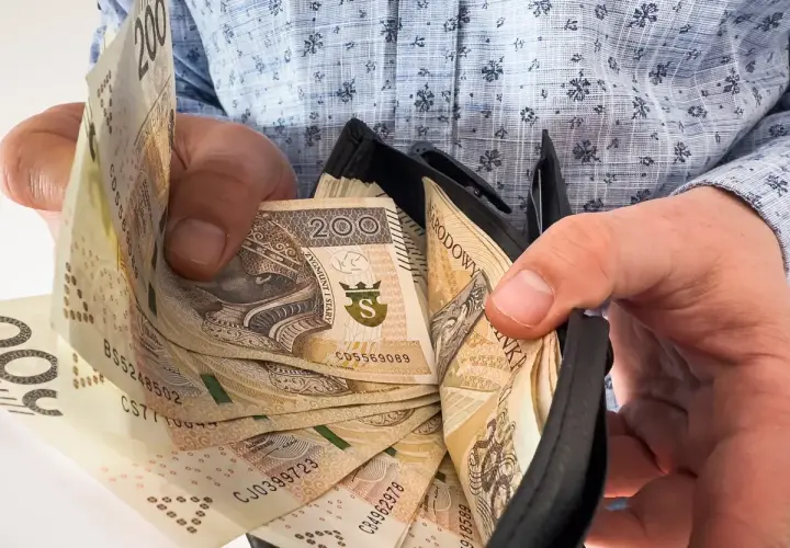 Dłonie trzymające portfel z polskimi banknotami 200 zł.