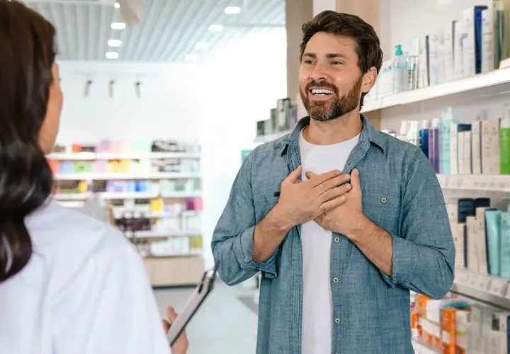 Mężczyzna z dłońmi na piersi rozmawia z farmaceutką, zastanawiając się, ile zarabia farmaceuta.