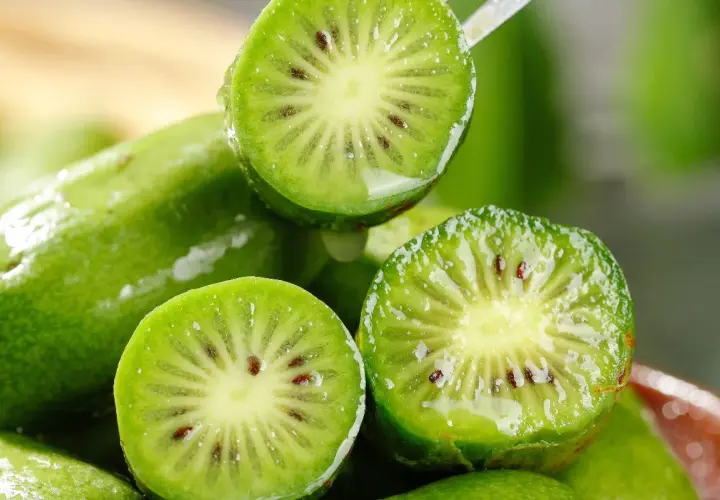 Przekrojone na pół, mokre kiwi z widocznymi pestkami na tle innych owoców.