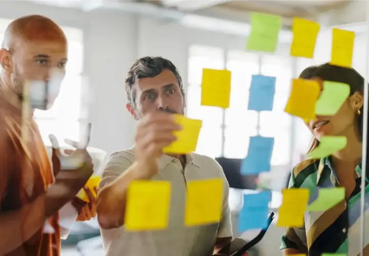 Zespół planuje strategię, wykorzystując karteczki samoprzylepne. Rozważają **outsourcing** zadań, by usprawnić proces.