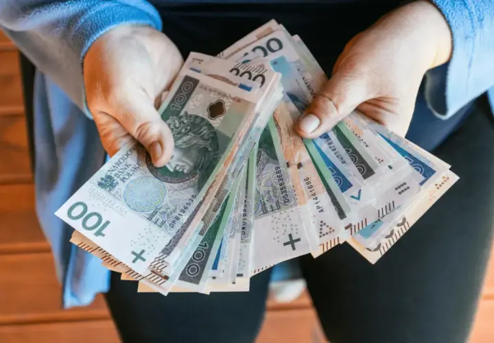 Dłonie trzymające plik polskich banknotów 100 zł.