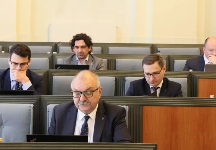 Mężczyźni w garniturach siedzą w rzędach, patrząc na laptopy.