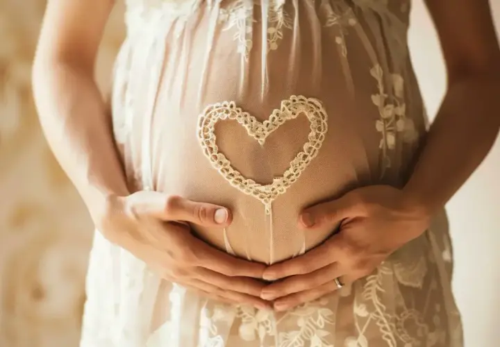 Brzuszek w 7 tygodniu ciąży, otulony koronkowym sercem. Dłonie mamy i taty czule obejmują przyszłe życie.