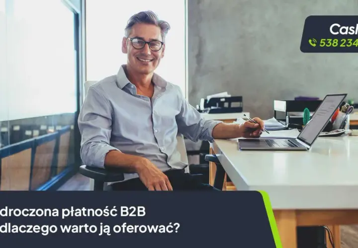 Uśmiechnięty mężczyzna w okularach siedzi przy biurku z laptopem, pisząc coś na papierze.