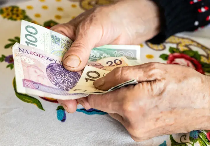 Dłonie starszej osoby liczą pieniądze. Może to być dodatek opiekuńczy po 80 roku życia, zapewniający wsparcie finansowe.
